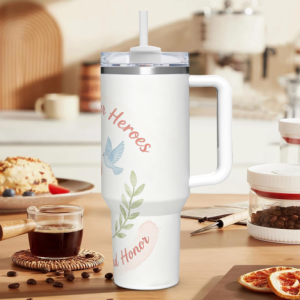 40oz Memorial Day handle tumbler with "Honoring Our Heroes" print, featuring watercolor-style red poppies, a dove, and "Remember and Honor" text, shown in a kitchen setting.