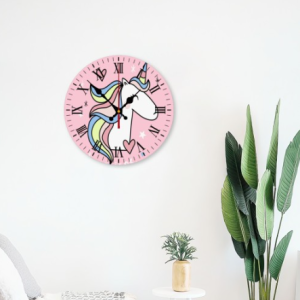 Pink round wall clock with a cute unicorn illustration, rainbow mane, and Roman numerals, hung on a bedroom wall next to a potted plant, perfect for kids' room decor.
