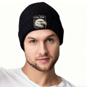 Black knit beanie with embroidered eagle design and “1776-2026” text, studio shot on a model.