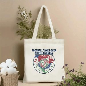 Front view of beige canvas tote bag featuring "Football Takes Over North America" slogan and a geometric emblem with North America map outline, tri-color patriotic accents (red, white, green), and soccer ball icon. Styled with dried botanicals, 2026 World Cup fan accessory.