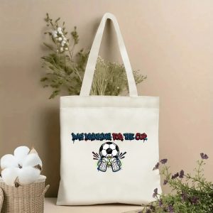 Front view of beige canvas tote bag with "Day Drinking For The Cup" graffiti-style slogan and a playful print featuring a soccer ball between two clinking beer mugs. Styled with cotton and dried botanicals, 2026 World Cup game day accessory.