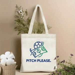 Front view of a beige canvas tote bag with a minimalist line-art graphic of a soccer ball and football pitch, paired with bold blue text "PITCH PLEASE." Styled with cotton stems and dried botanicals, perfect for 2026 World Cup soccer fans.
