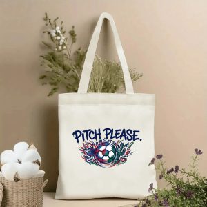 Front view of a beige canvas tote bag featuring a vibrant 2026 World Cup design. The central graphic includes the playful slogan "PITCH PLEASE." in bold blue graffiti-style lettering, with a stylized soccer ball surrounded by Canadian maple leaf, Mexican cactus, and patriotic red, white, and blue flame motifs, set against a neutral beige background with cotton stems.