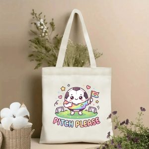 Front view of a beige canvas tote bag featuring a cute 2026 World Cup kawaii design. The central graphic is a chibi-style anthropomorphic soccer ball character in a rainbow shirt, holding a pride flag, surrounded by stars and hearts, with the playful slogan "PITCH PLEASE" in rainbow lettering, styled with cotton stems and dried botanicals.