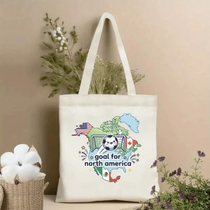 Front view of a beige tote bag with a cheerful 2026 World Cup print. Features a cartoon soccer ball in a goal, North America map outline, USA/Canada/Mexico flags, fireworks, and the text "goal for north america".