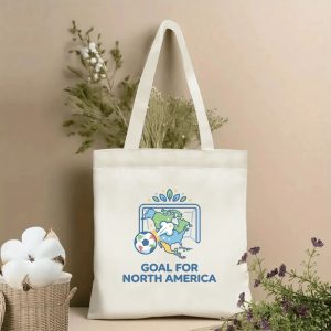 Front view of a beige canvas tote bag with a cute 2026 World Cup design. Features a cartoon soccer ball striking a North America map goal net, green leaf decor, stars, and the bold "GOAL FOR NORTH AMERICA" text in navy blue, styled with cotton stems and dried botanicals.