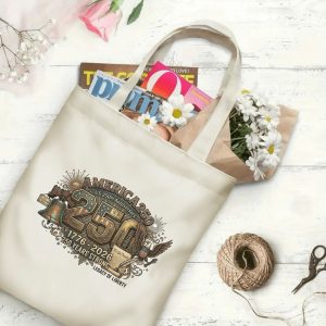 Canvas tote bag with the same America 250th print, shown open with books and flowers inside, on a white wooden surface.