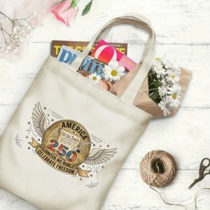 Canvas tote bag with the same America 250th print, shown open with books and flowers inside, on a white wooden surface.