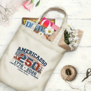 Canvas tote bag with the same America 250th print, shown open with books and flowers inside, on a white wooden surface.