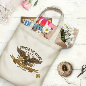 Canvas tote bag with the same America 250th print, shown open with books and flowers inside, on a white wooden surface.