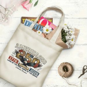 Canvas tote bag with the same America 250th print, shown open with books and flowers inside, on a white wooden surface.