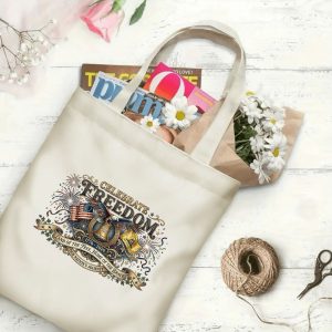 Canvas tote bag with the same America 250th print, shown open with books and flowers inside, on a white wooden surface.