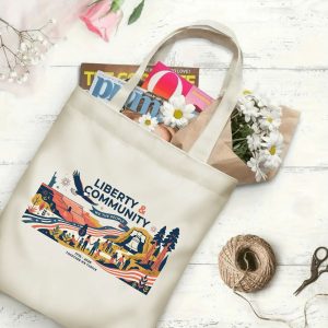 Canvas tote bag with the same America 250th print, shown open with books and flowers inside, on a white wooden surface.