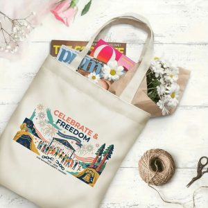 Canvas tote bag with the same America 250th print, shown open with books and flowers inside, on a white wooden surface.