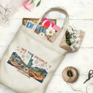 Canvas tote bag with the same America 250th print, shown open with books and flowers inside, on a white wooden surface.