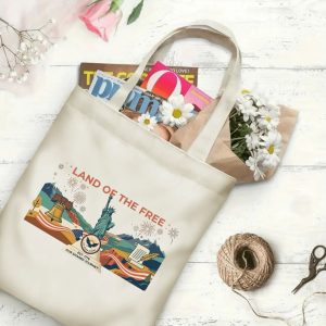 Canvas tote bag with the same America 250th print, shown open with books and flowers inside, on a white wooden surface.