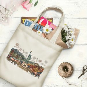 Canvas tote bag with the same America 250th print, shown open with books and flowers inside, on a white wooden surface.