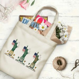 Canvas tote bag with the same America 250th print, shown open with books and flowers inside, on a white wooden surface.