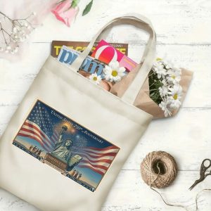 Canvas tote bag with the same America 250th print, shown open with books and flowers inside, on a white wooden surface.