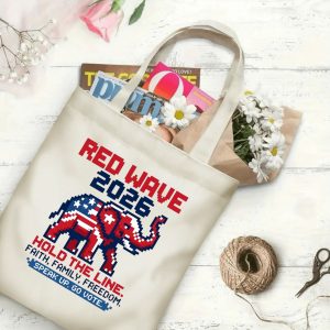 Natural canvas tote bag with a "Red Wave 2026" pixel graphic print, shown open with magazines and flowers inside, placed on a white wooden background.