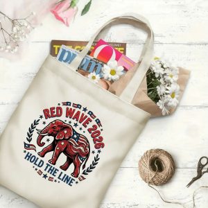 Natural canvas tote bag with a "Red Wave 2026" graphic print, shown open with magazines and flowers inside, placed on a white wooden background. The design features a Republican elephant surrounded by stars and a laurel wreath.