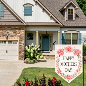 Outdoor scene of a suburban house with a decorated "Happy Mother's Day" garden flag (pink peony floral design) displayed on a black stand, showcasing the final printed look.