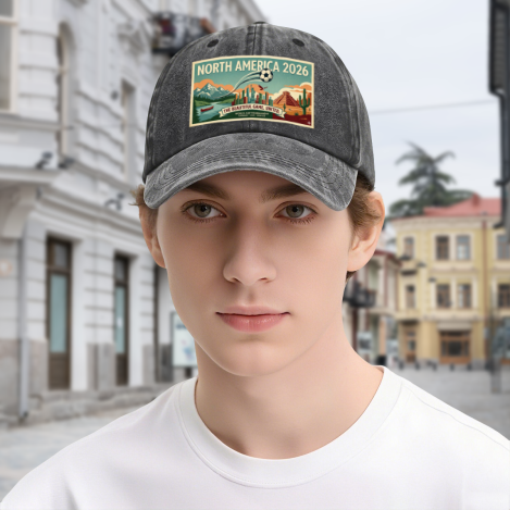 Young man wearing dark grey vintage washed North America 2026 landscape‑poster dad hat, outdoor street‑style portrait of 2026 World Cup soccer fan with casual retro headwear