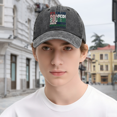 Young man wearing dark gray vintage‑washed adjustable dad hat, front retro multi‑color distressed “It’s Called Soccer! North America United” stacked‑text typography print, street‑style outdoor lifestyle shot, unisex 2026 World Cup sports baseball cap