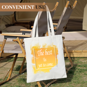 “The best is yet to come” tote bag on an outdoor camping chair, showcasing the yellow watercolor print in a casual setting.
