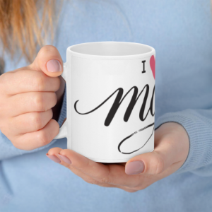 A white 11oz ceramic coffee mug held in hands, featuring elegant black cursive "mom" text with "I ❤️ U" and delicate pink flowers.