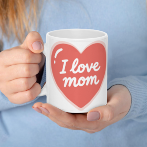 A white 11oz ceramic coffee mug held in hands, featuring a large coral heart with white cursive text reading "I love mom".
