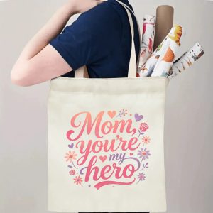 A person carrying the "Mom, you're my hero" print canvas tote bag over their shoulder, showing its comfortable straps and roomy design with rolled papers inside.