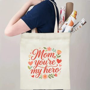 A person carrying the "Mom, you're my hero" print canvas tote bag over their shoulder, showing its comfortable straps and roomy design with rolled papers inside.