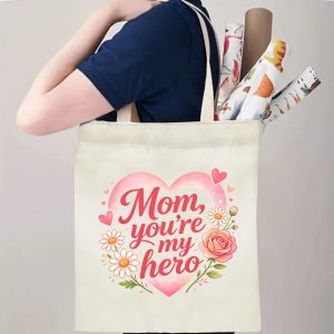 A person carrying the "Mom, you're my hero" heart print canvas tote bag over their shoulder, showing its comfortable straps and roomy design with rolled papers inside.