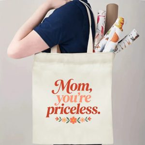 A person carrying the "Mom, you're priceless." print canvas tote bag over their shoulder, showing its comfortable straps and roomy design with rolled papers inside.