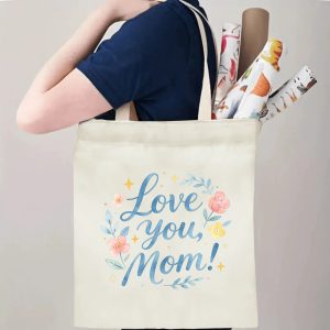A person carrying the "Love you, Mom!" print canvas tote bag over their shoulder, showing its comfortable straps and roomy design with rolled papers inside.