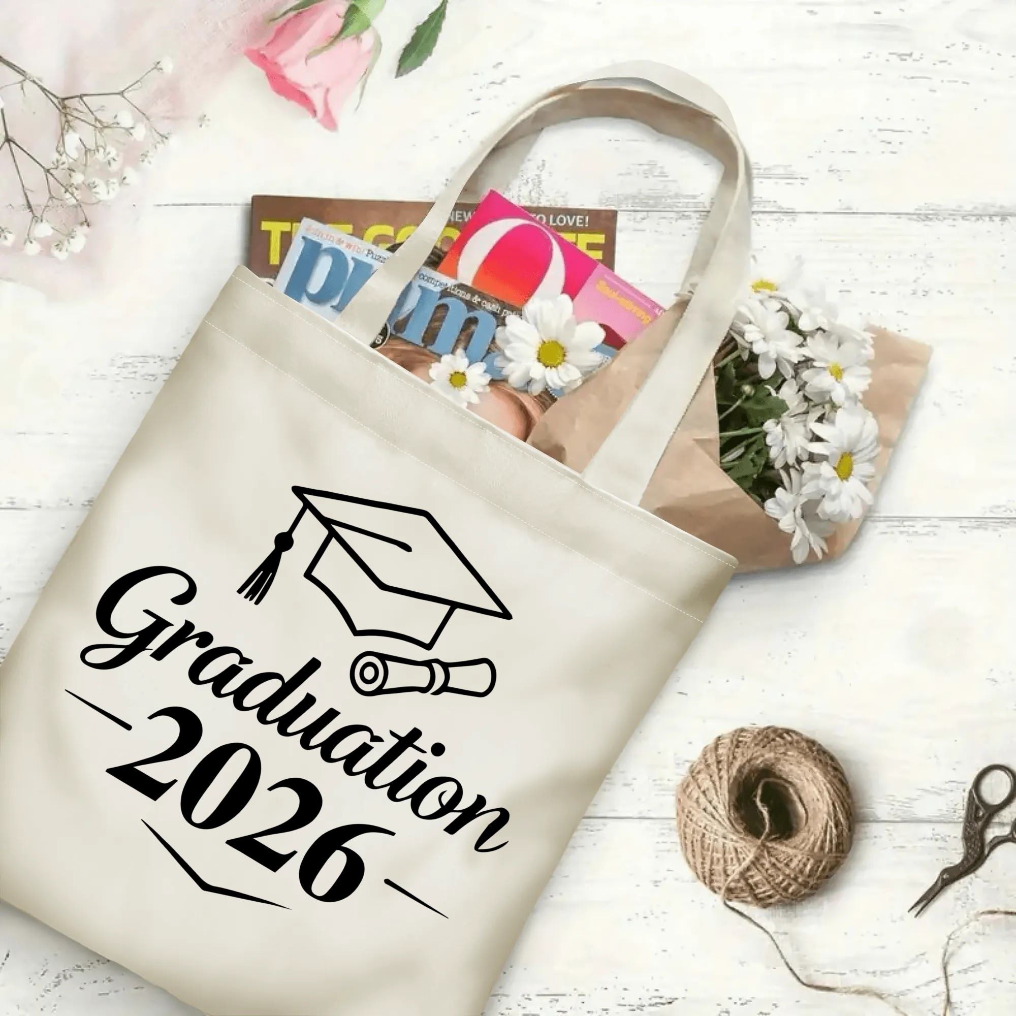 2026 Graduation beige canvas tote bag with cap‑and‑diploma graphic, flat lay styled with daisies, books and twine, graduation gift bag