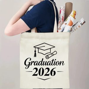 Person carrying beige 2026 Graduation canvas tote bag with graduation cap print, casual outdoor graduation gift‑style reusable shopping bag