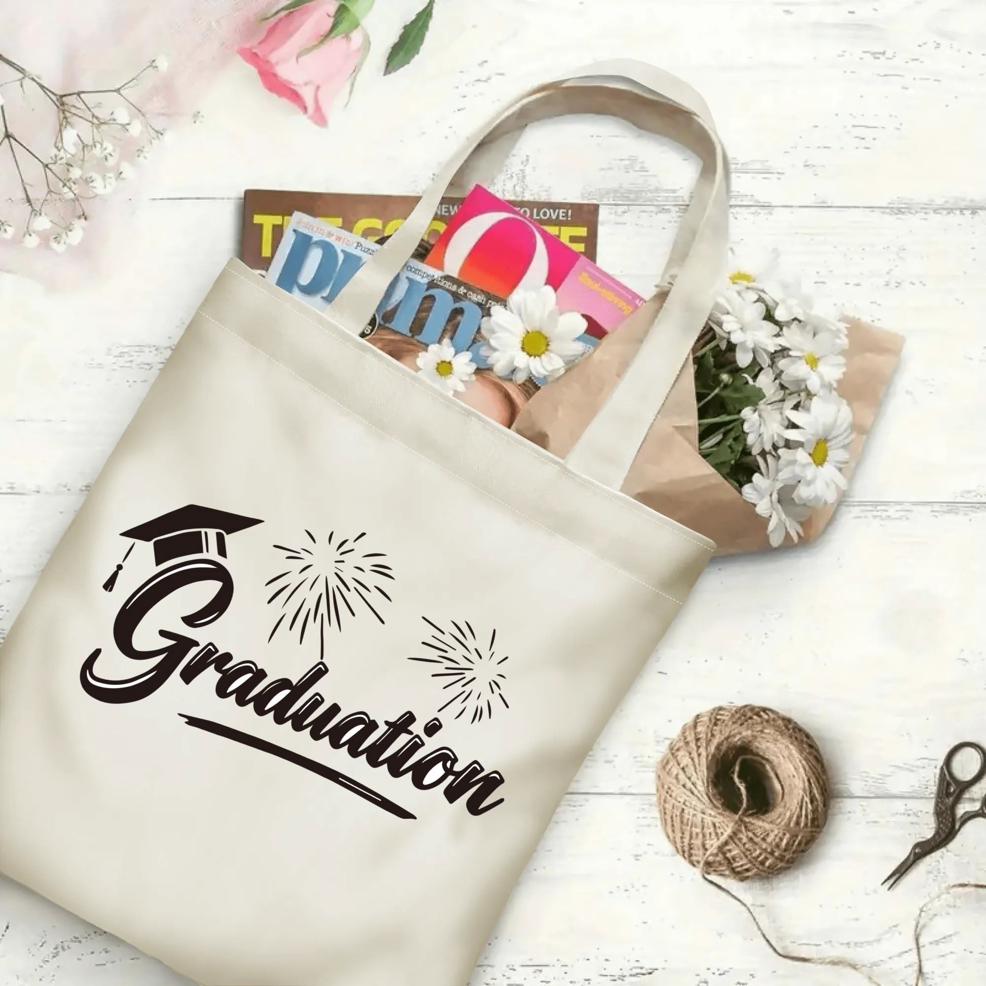 Flat‑lay shot of natural canvas graduation tote bag with graduation cap, fireworks and "Graduation" cursive print, decorated with daisies and books, ideal graduation gift