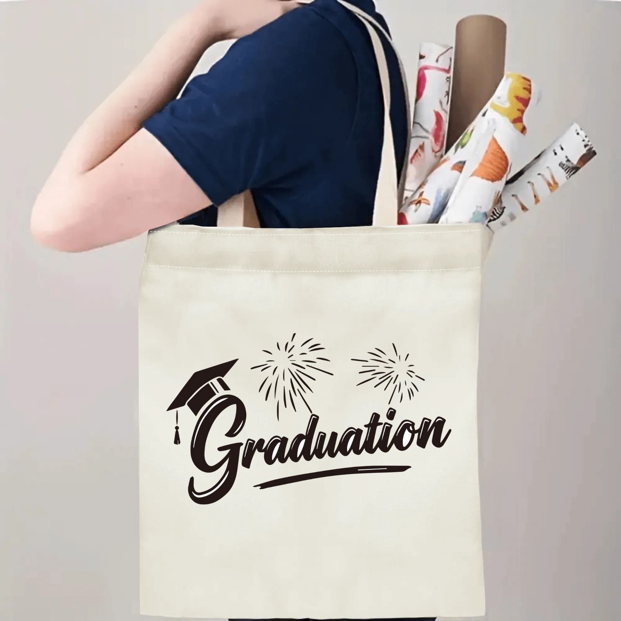 Person carrying natural canvas graduation tote bag with graduation cap, fireworks and "Graduation" cursive print, casual graduation‑day reusable gift bag
