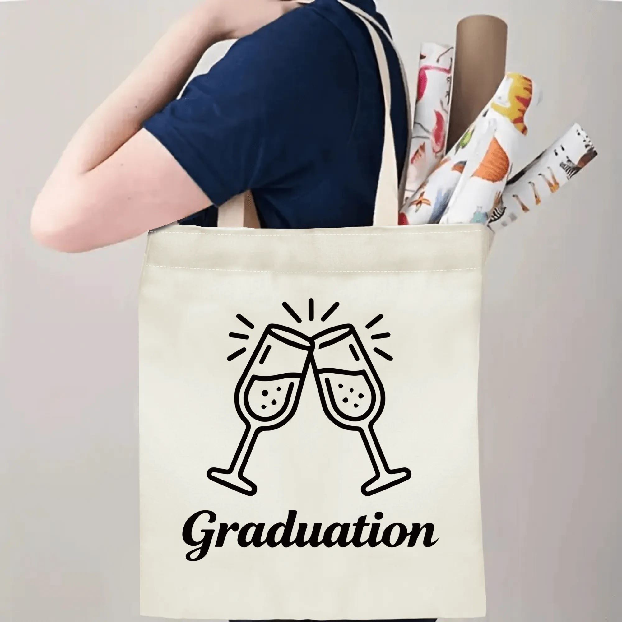 Person carrying natural canvas graduation tote bag with clinking champagne glasses and "Graduation" cursive print, casual celebration‑style reusable gift bag