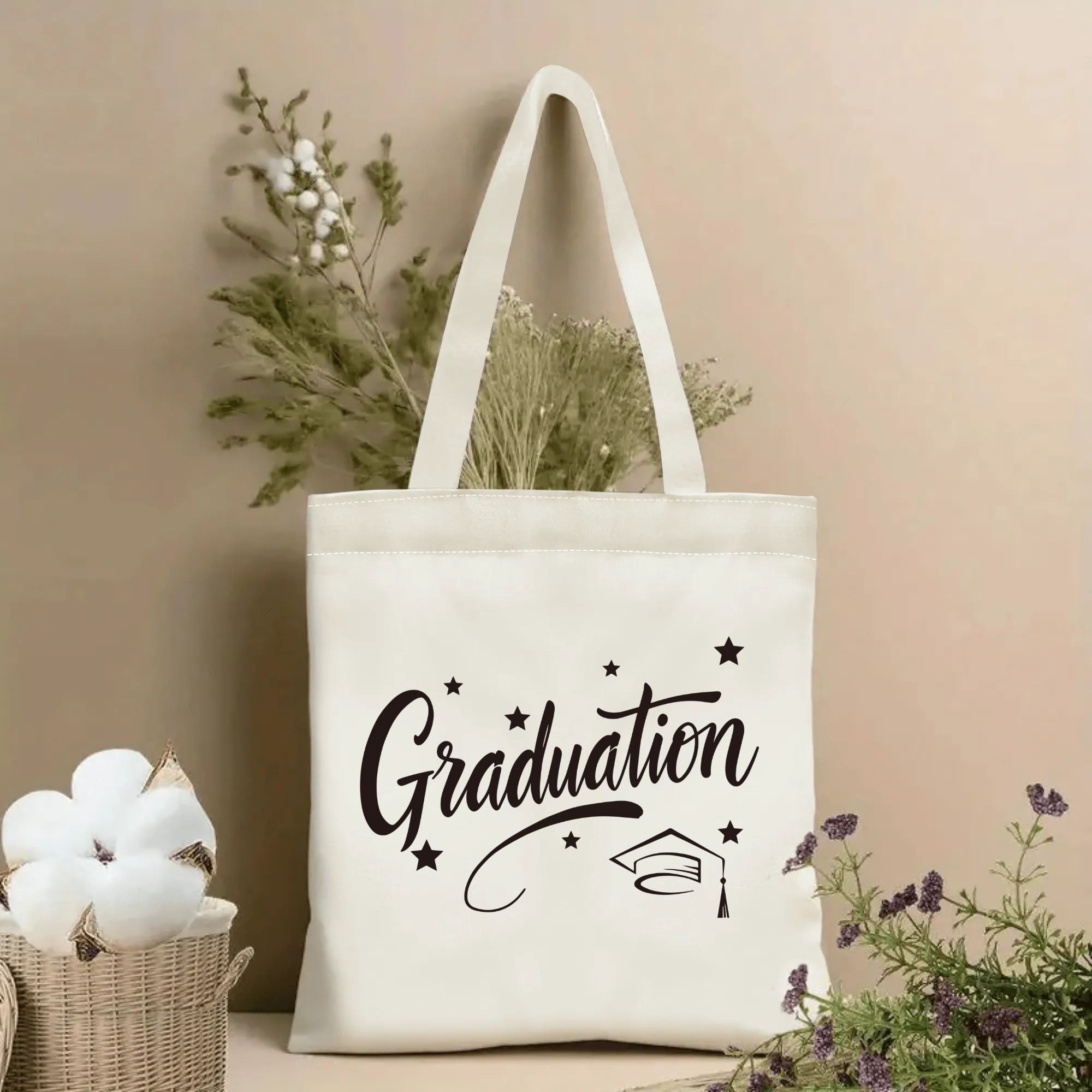 Natural canvas graduation‑themed tote bag featuring cursive "Graduation" lettering, graduation cap and scattered star print, styled with dried flowers for graduation gift display