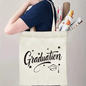 Person carrying natural canvas graduation tote bag with cursive "Graduation", graduation cap and star print, casual milestone‑celebrating reusable gift bag
