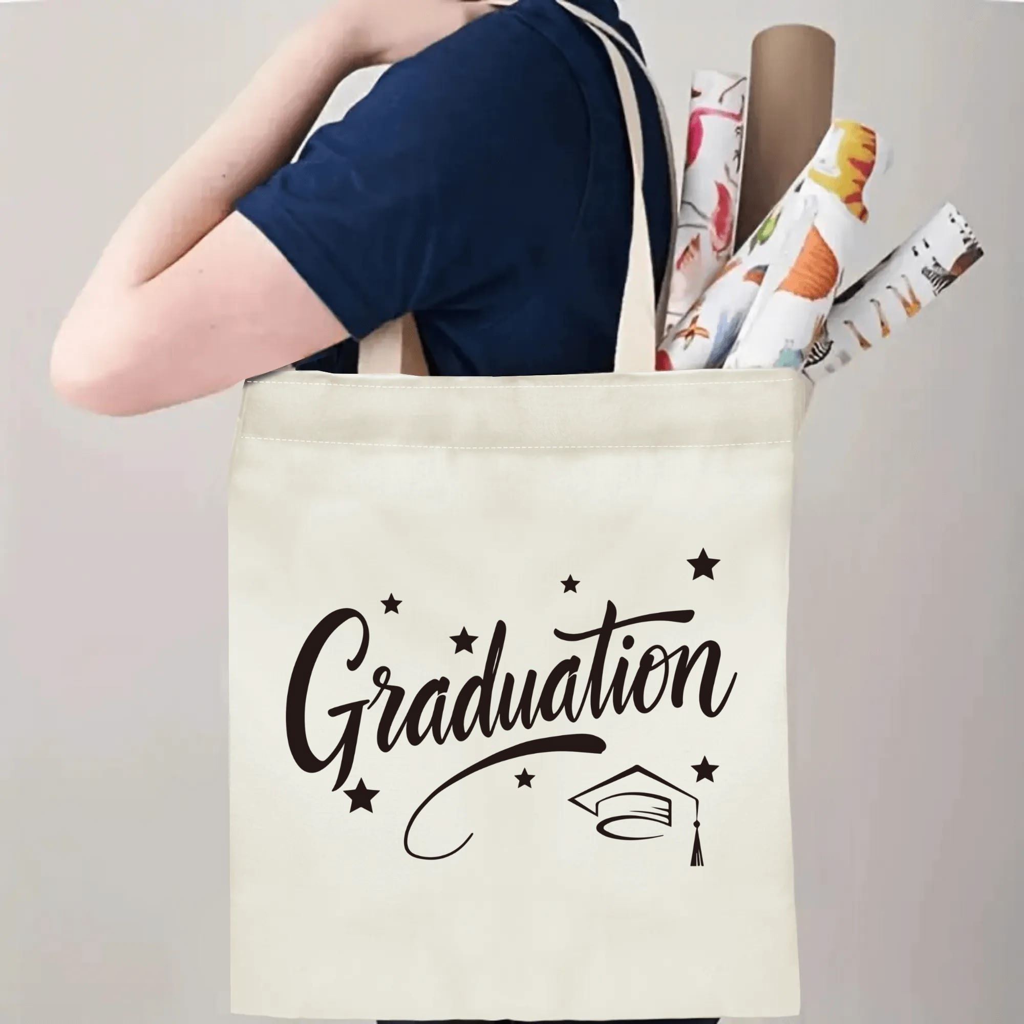 Person carrying natural canvas graduation tote bag with cursive "Graduation", graduation cap and star print, casual milestone‑celebrating reusable gift bag
