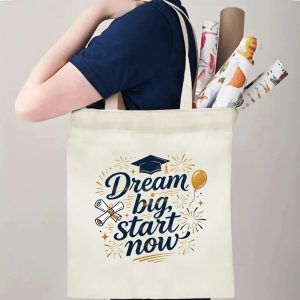 Person carrying natural canvas graduation tote bag with "Dream big, start now" motivational quote, graduation cap, diploma and fireworks print, casual milestone‑celebrating reusable gift bag