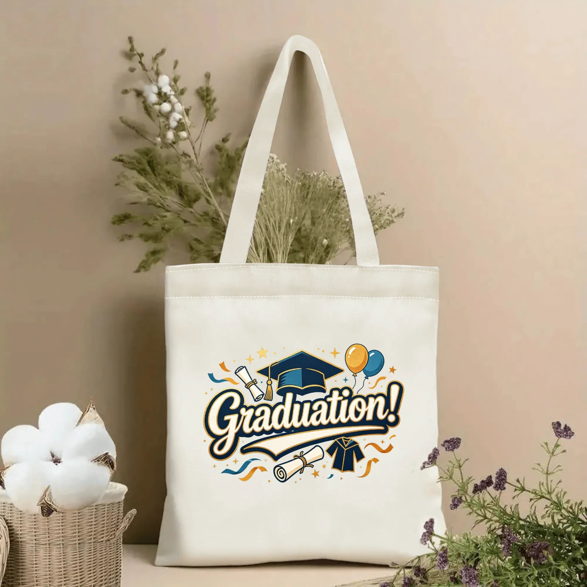 Natural canvas graduation‑themed tote bag featuring bold "Graduation!" cursive lettering, decorated with graduation cap, diploma, graduation gown, colorful balloons, confetti and stars, styled with dried flowers for graduation gift display
