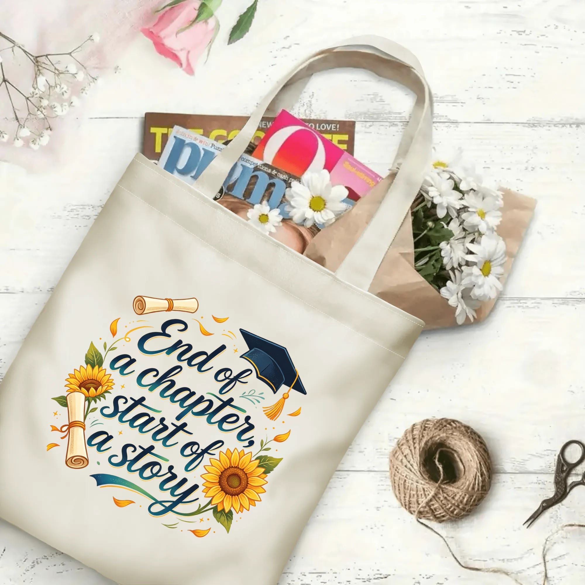 Flat‑lay shot of natural canvas graduation tote bag with sentimental "End of a chapter, start of a story" print, graduation cap, diploma and sunflower accents, decorated with daisies and books, ideal graduation gift