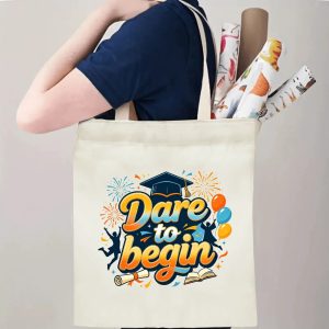 Person carrying natural canvas graduation tote bag with upbeat "Dare to begin" gradient‑colored print, graduation cap and joyful graduate graphics, casual milestone‑celebrating reusable gift bag