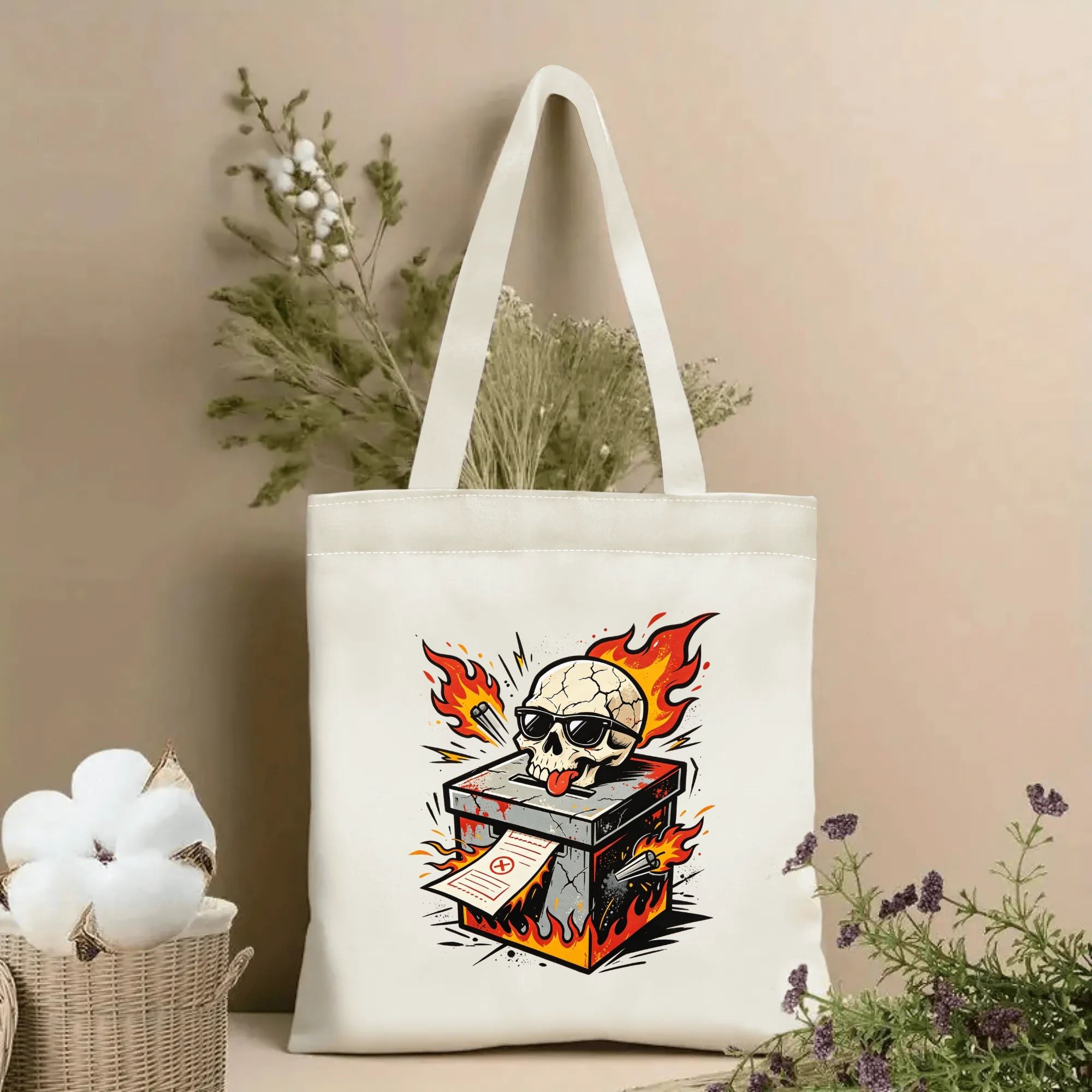 Natural canvas 2026 US mid‑term election themed tote bag featuring an edgy traditional tattoo‑style skull wearing sunglasses popping out of a fiery cracked ballot box, with flaming accents, bullet details and voting slip graphic, styled with dried flowers for voting‑season gift display