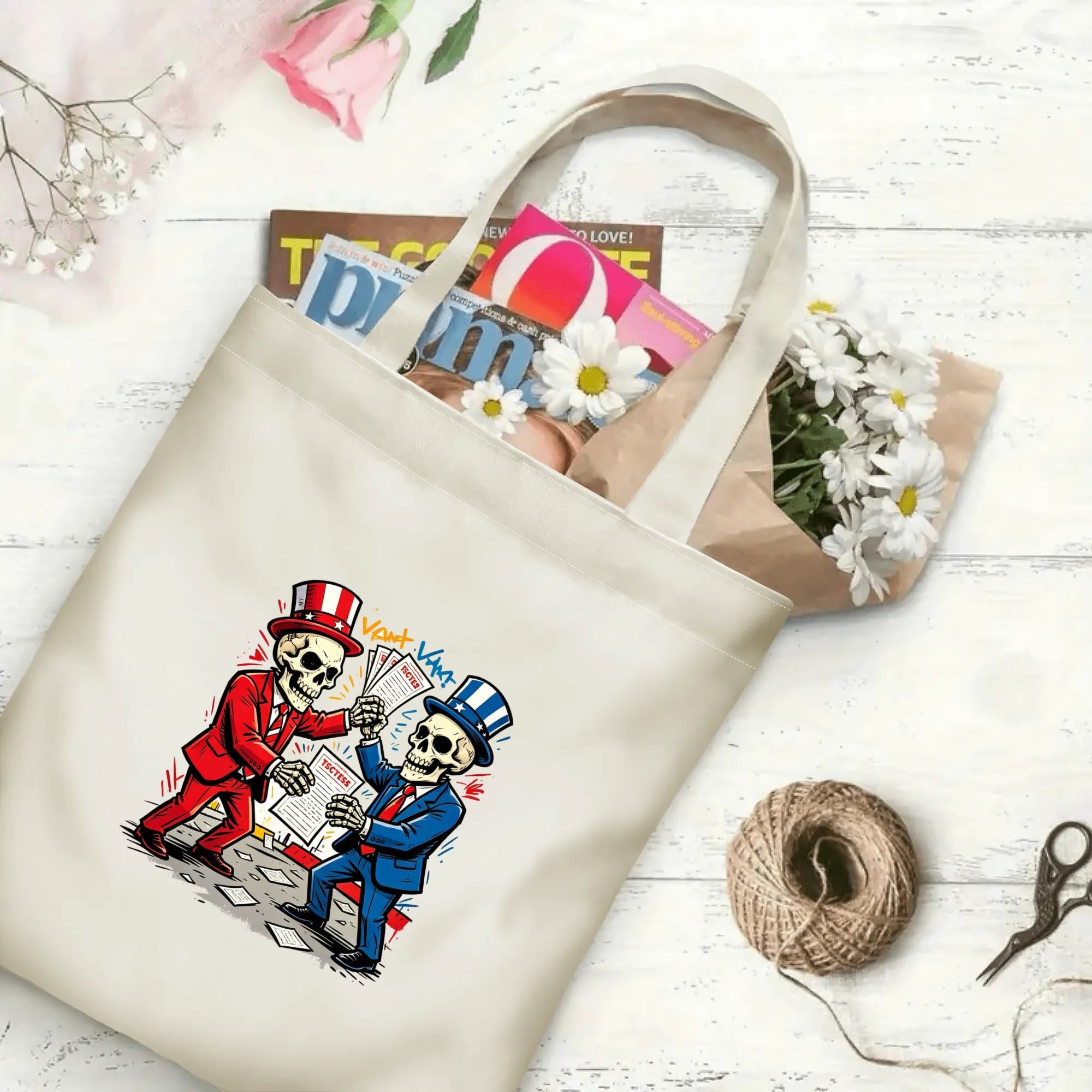 Flat‑lay shot of natural canvas political novelty tote bag with fun retro‑cartoon bipartisan skull Uncle Sam graphic, red‑blue party colors and voting‑document details, decorated with daisies, ideal casual daily‑wear bag for voters